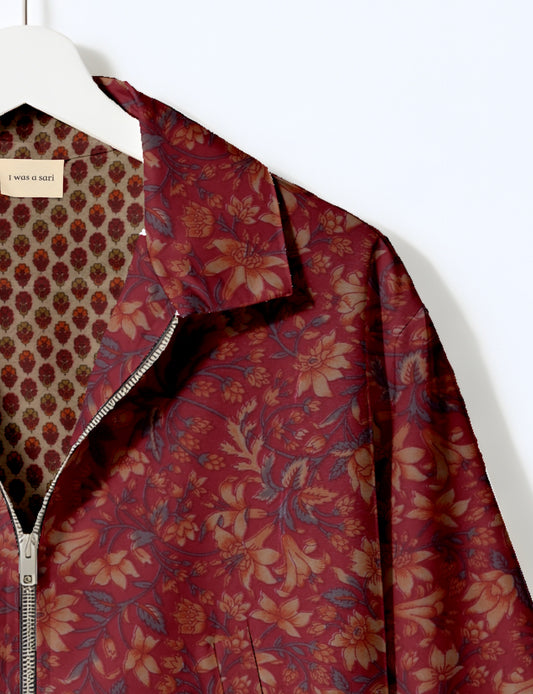 Red floral patterned bomber jacket with silver zipper, shown on hanger with inner beige floral lining and label "I was a sari"