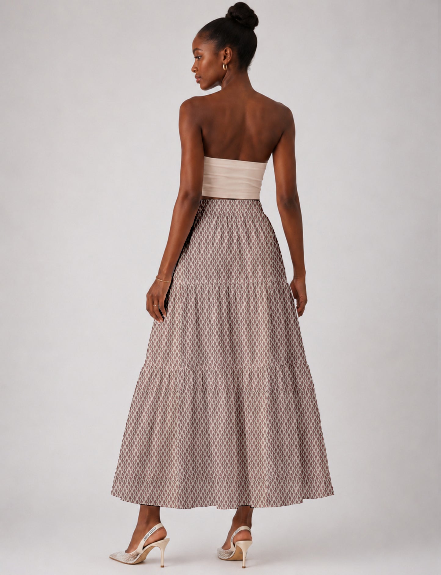 Woman wearing a yellow midi tiered skirt with a small geometric pattern, paired with a beige strapless top and white heels