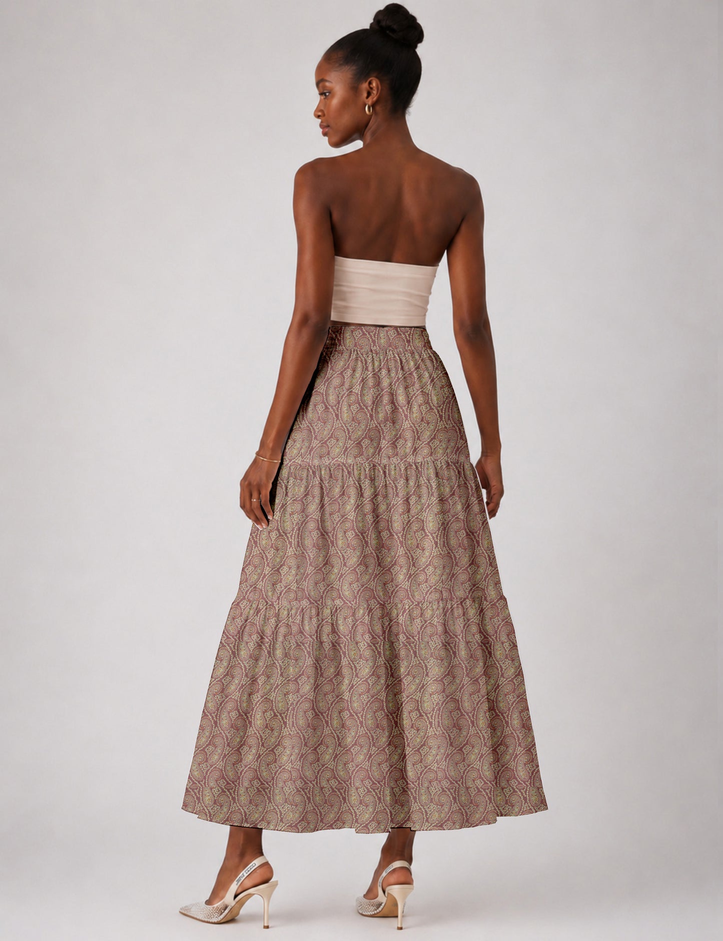 Woman wearing a yellow midi tiered skirt with a small geometric pattern, paired with a beige strapless top and white heels