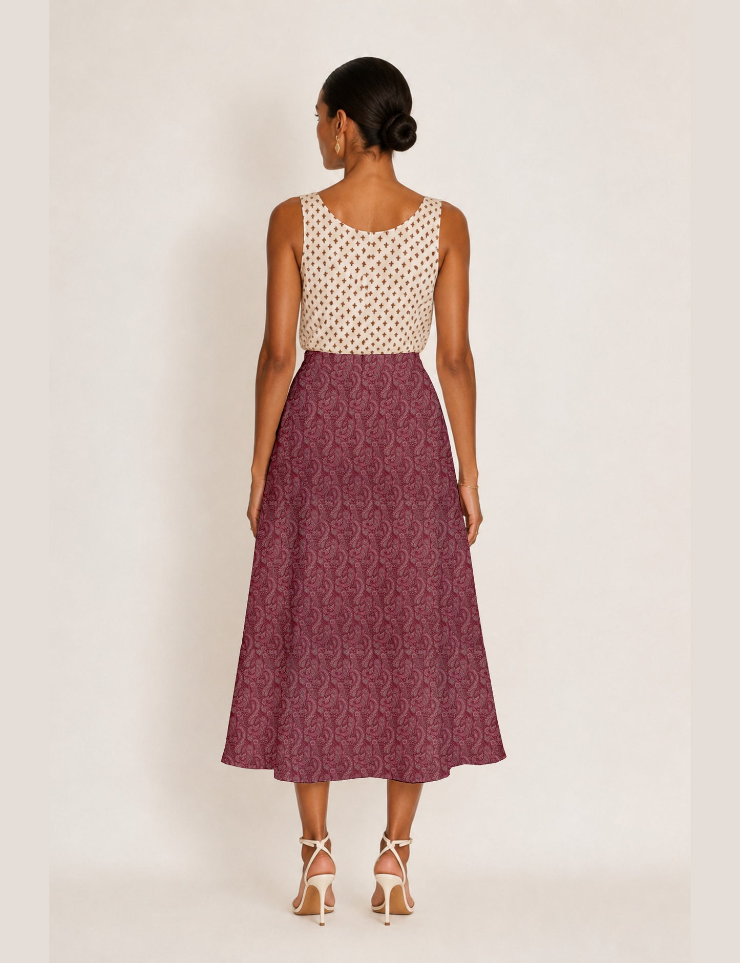Woman wearing a yellow and black micro patterned A-line skirt with front slit, paired with beige sleeveless top and black