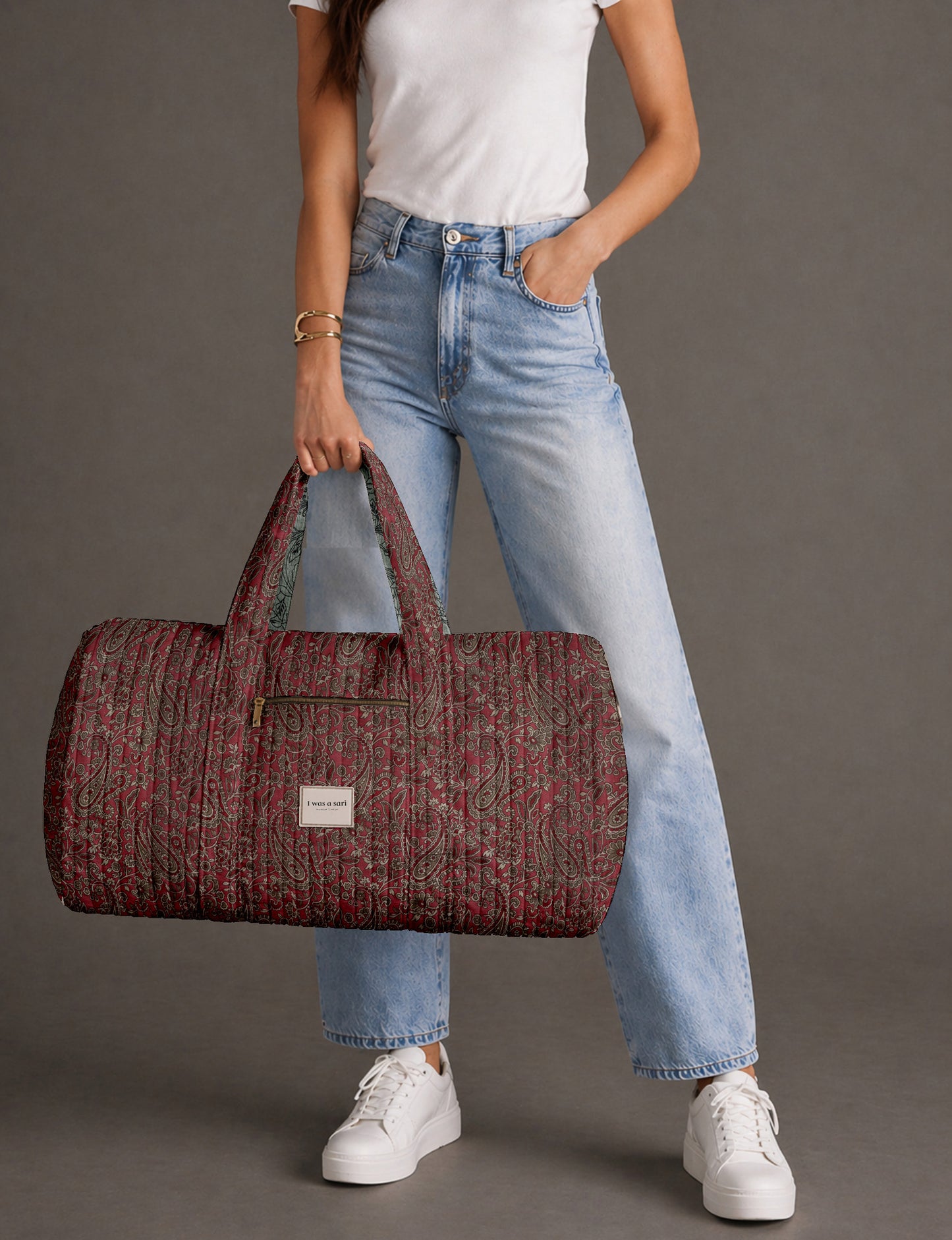 Quilted brown paisley barrel bag with double handles, front pocket, and gold zipper, shown in side angle view