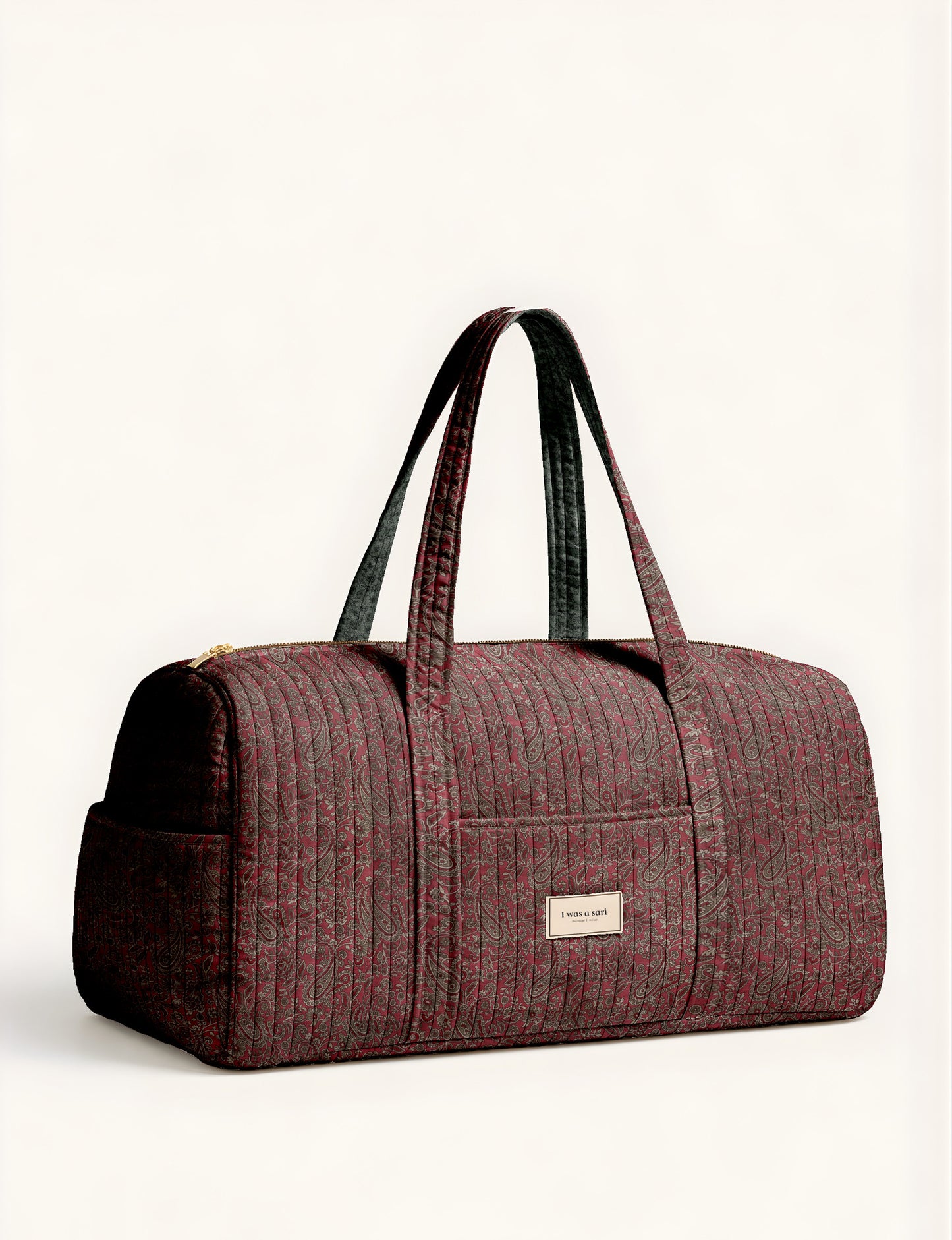 Woman holding a brown paisley quilted barrel bag with front zipper pocket, wearing light blue jeans and white sneakers