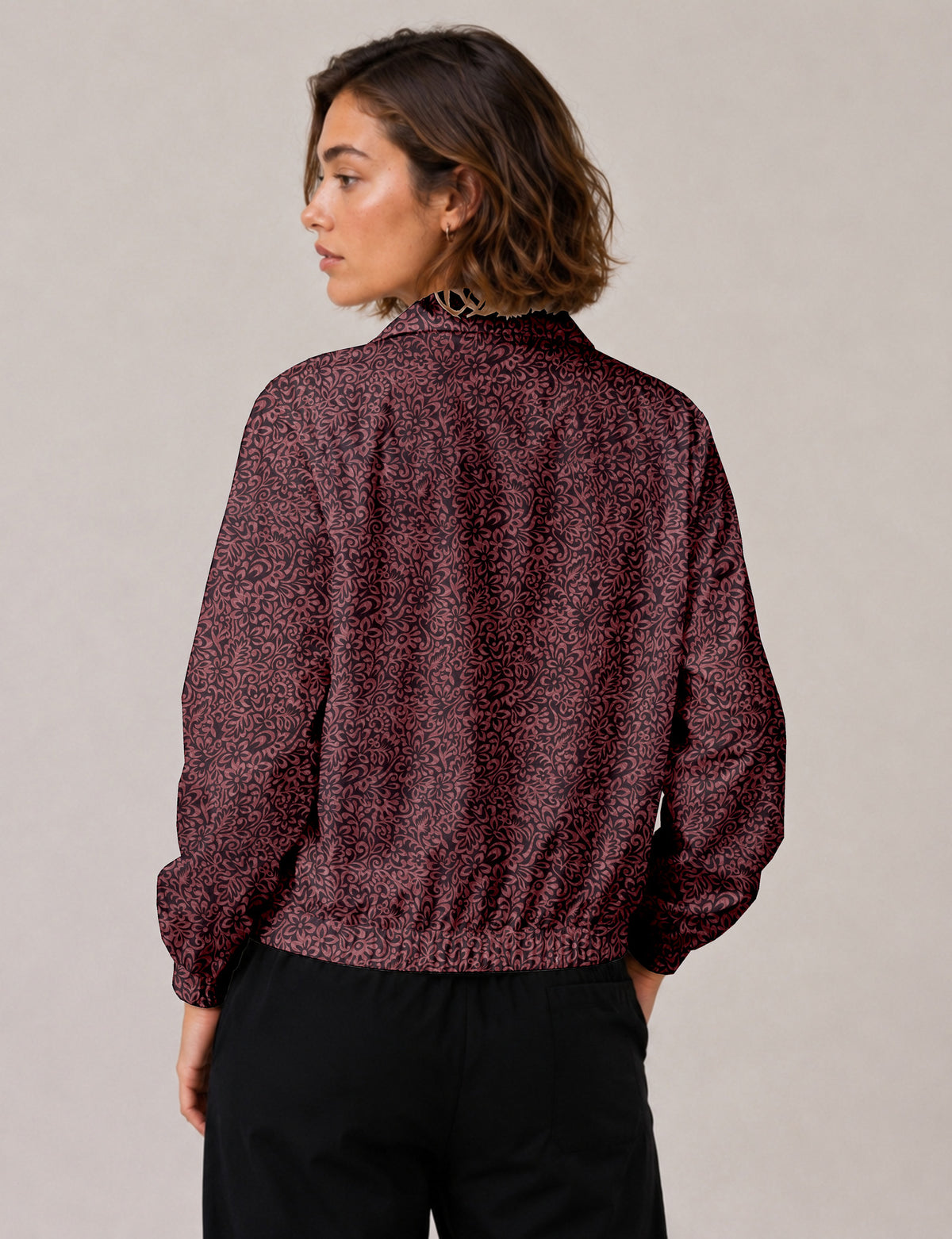 Brown floral bomber jacket with front zipper, elastic cuffs and hem, hanging on white hanger, red floral inner lining visible