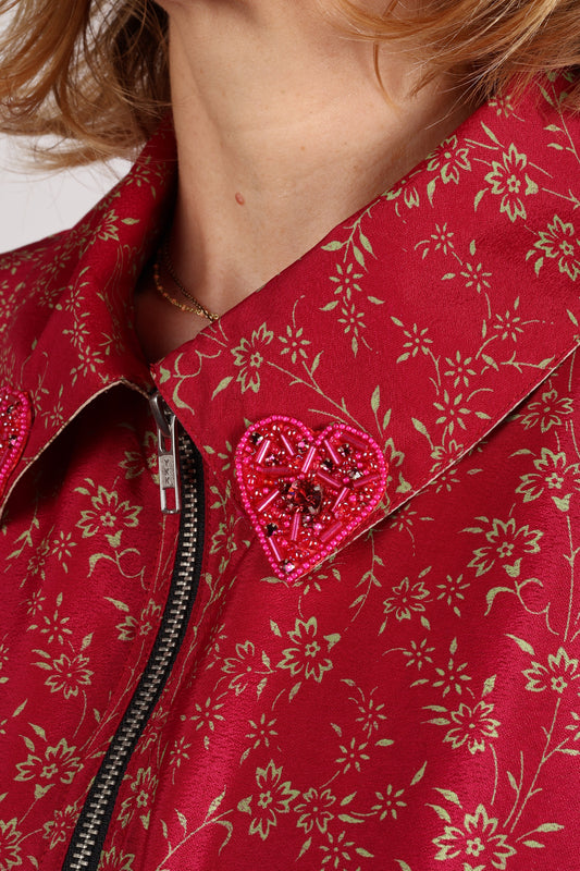Red bomber jacket with green floral paisley print, front zipper, and pink beaded heart embellishment on collar, worn by model