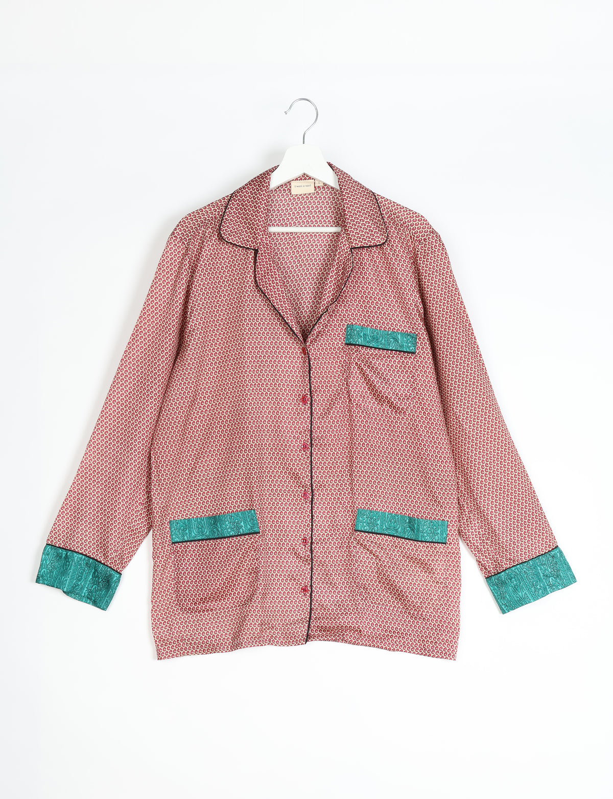 Beige long-sleeve pajama top with red micro pattern, teal paisley pocket and cuff accents, black piping, hanging on white hanger