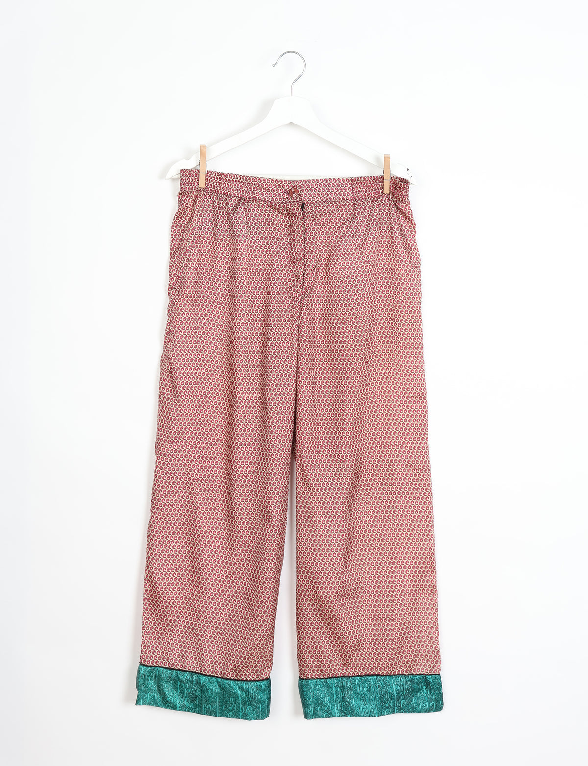 Beige pajama pants with red micro crescent pattern and teal paisley cuffs hanging on white hanger against white background