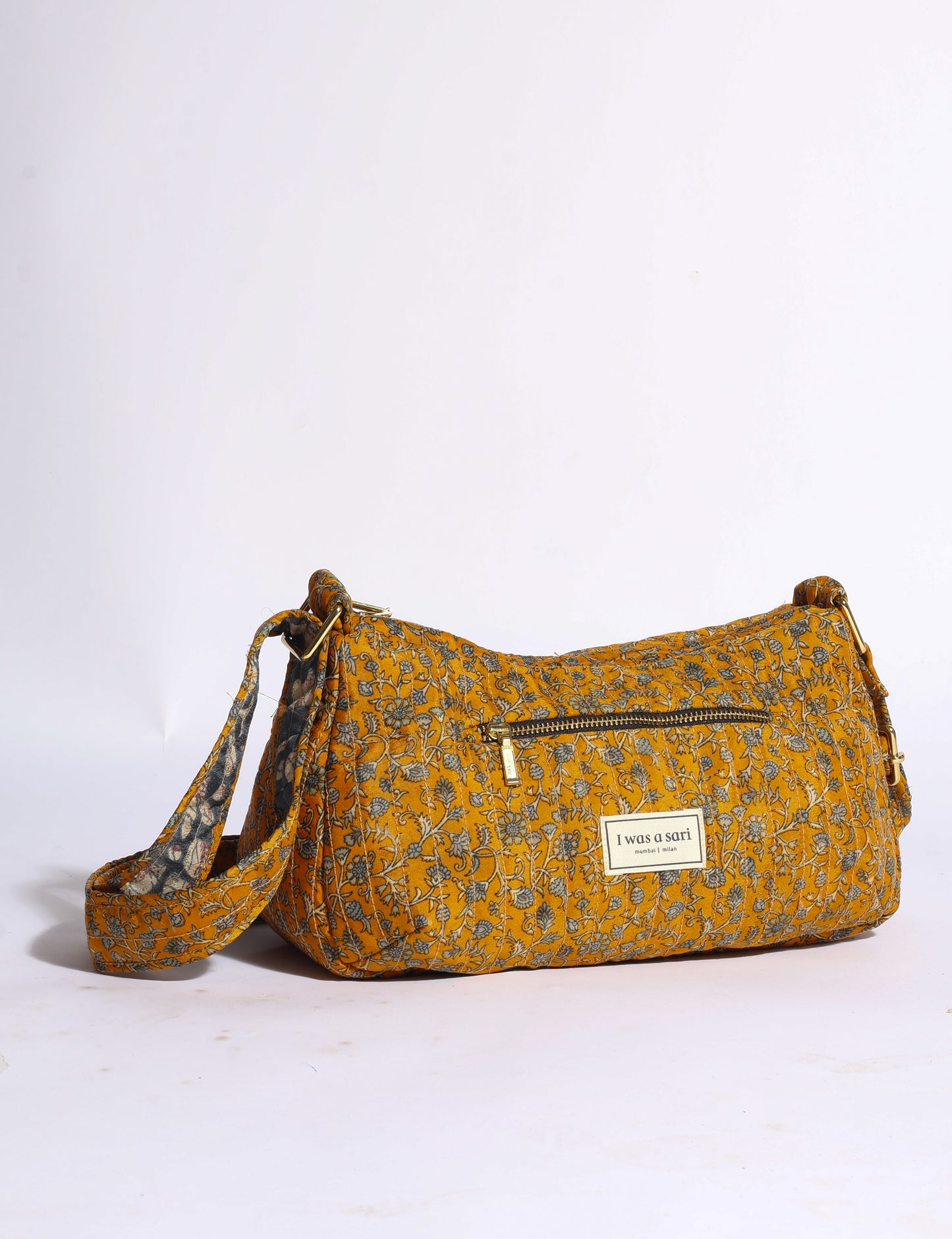 Quilted mustard yellow sling bag with floral print, front zipper pocket, adjustable strap, and "I was a sari" label