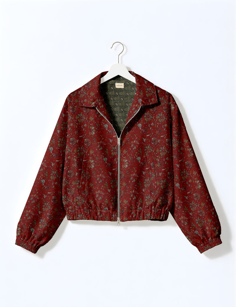 Brown floral bomber jacket with front zipper, elastic cuffs and hem, hanging on white hanger, red floral inner lining visible