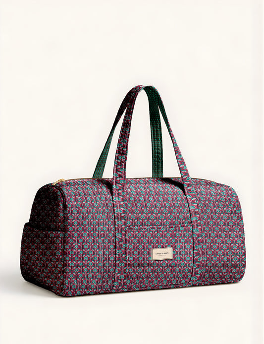 Quilted brown paisley barrel bag with double handles, front pocket, and gold zipper, shown in side angle view