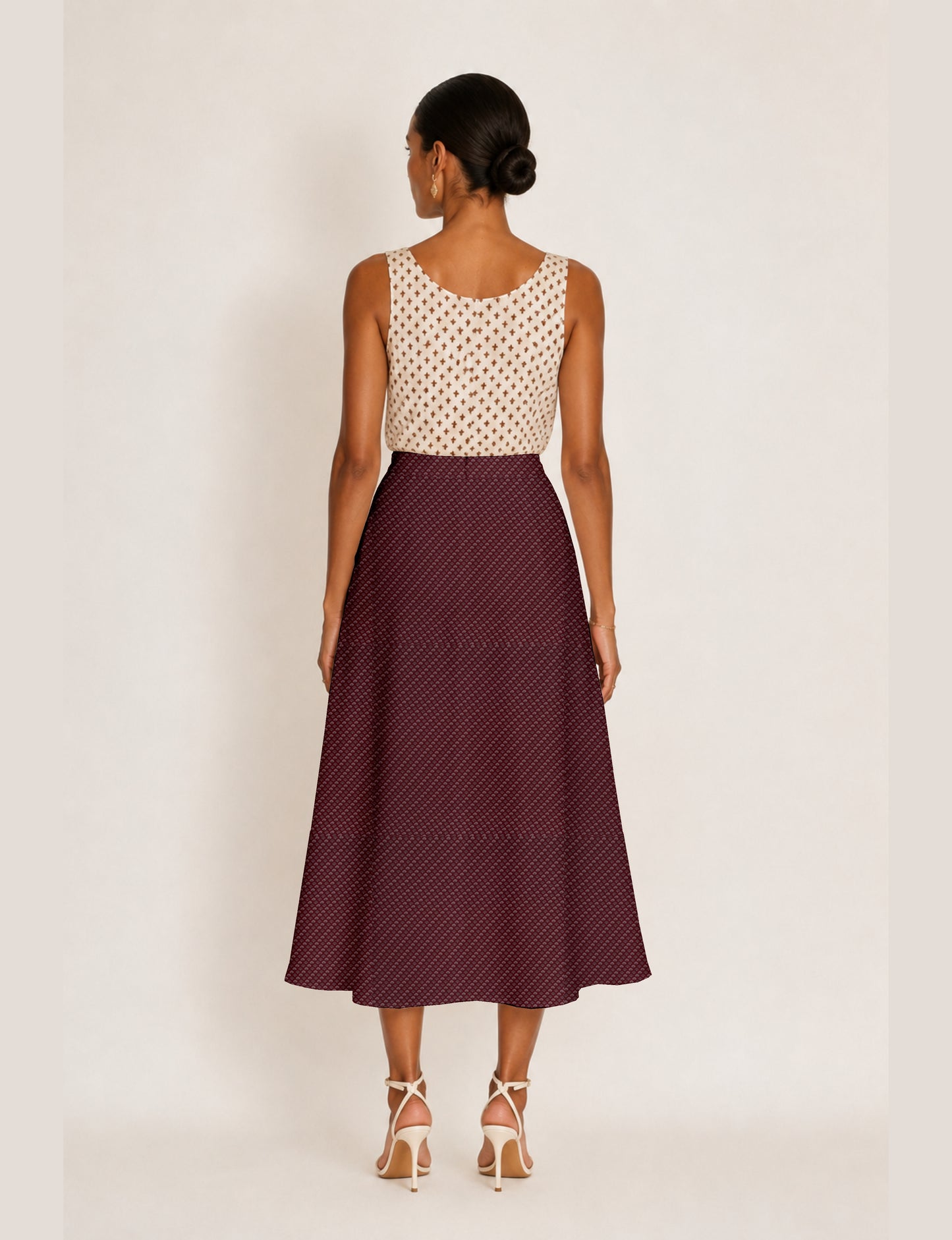 Woman wearing a yellow micro design A-line skirt with side slit, paired with a sleeveless beige top with small cross