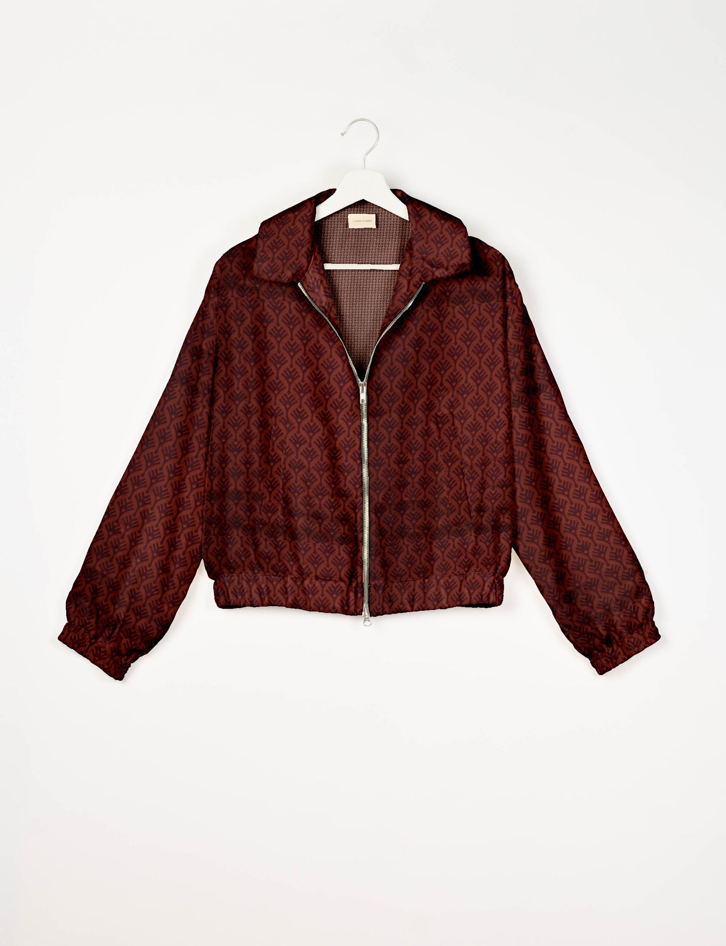 Red bomber jacket with dark red leaf pattern, front zipper, elastic cuffs and hem, hanging on white hanger front view