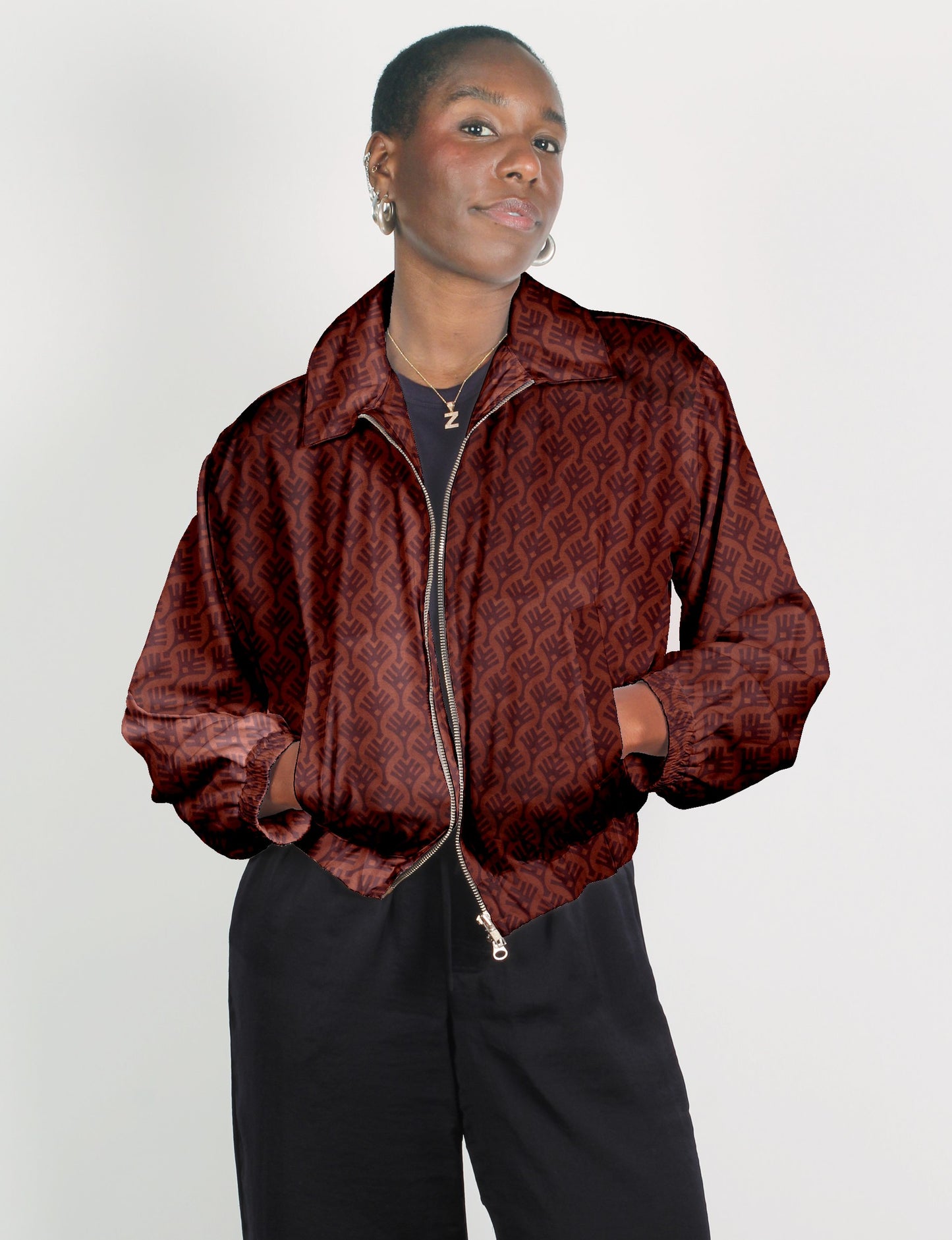 Model wearing a red bomber jacket with dark leaf pattern, front zipper, elastic cuffs, and collar, paired with black pants