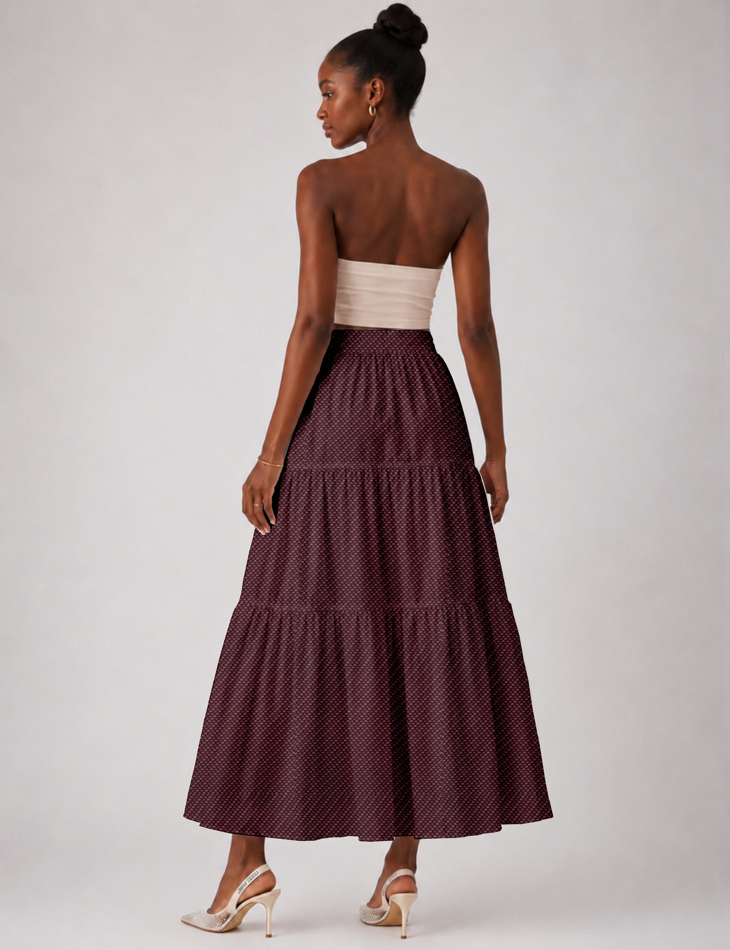 Woman wearing a yellow midi tiered skirt with a small geometric pattern, paired with a beige strapless top and white heels