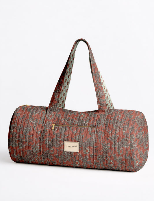 Quilted bowling bag by I Was A Sari with a structured design, featuring dual handles, zip closure, and a spacious interior with an outer zip pocket. Designed for everyday use and travel, it showcases a sleek elongated silhouette with functional storage and easy access compartments. Made from upcycled fabric, this sustainable handbag combines style and practicality, presented through detailed front, side, and lifestyle views.