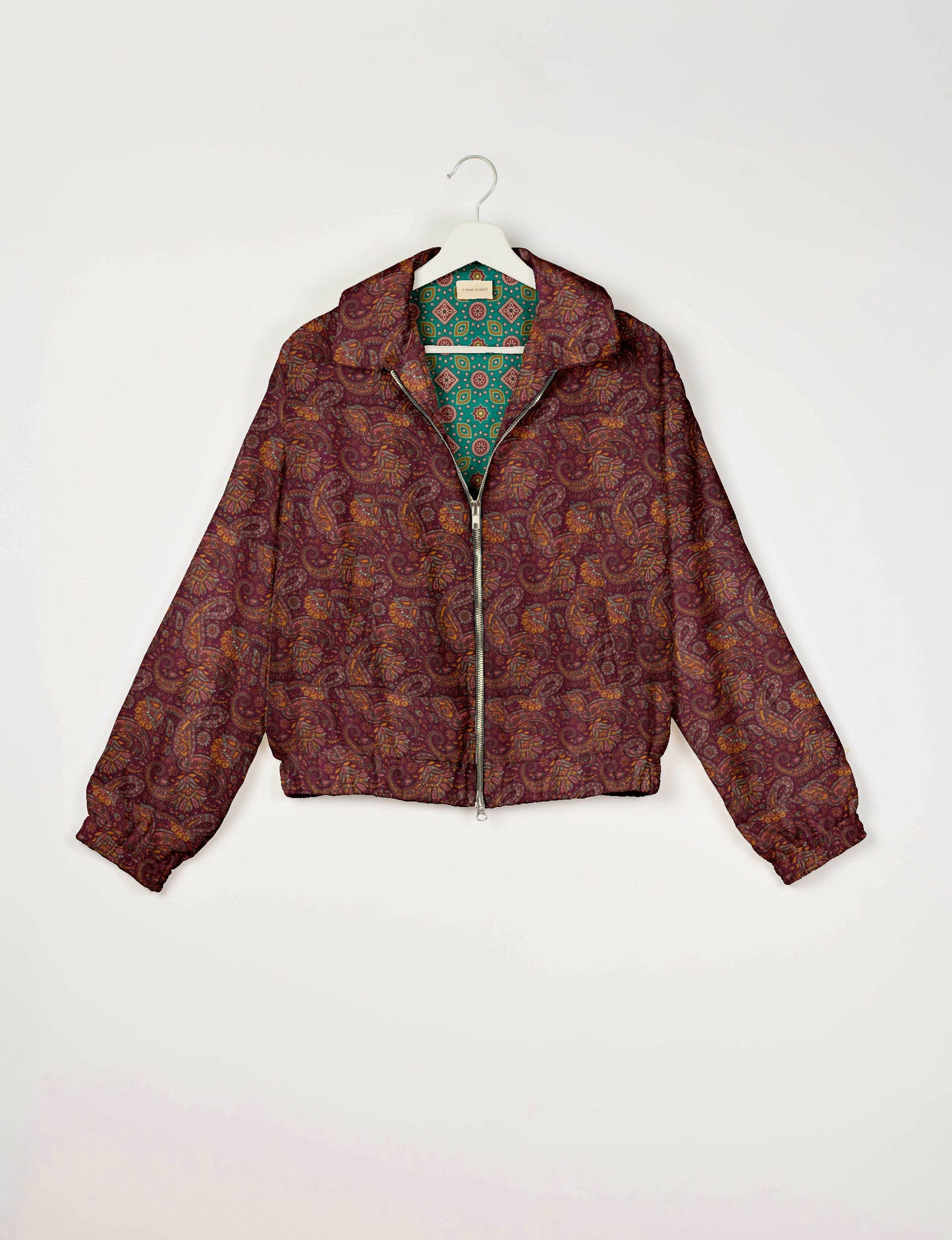 Red paisley bomber jacket with front zipper, elastic cuffs and waistband, shown hanging with green patterned lining visible