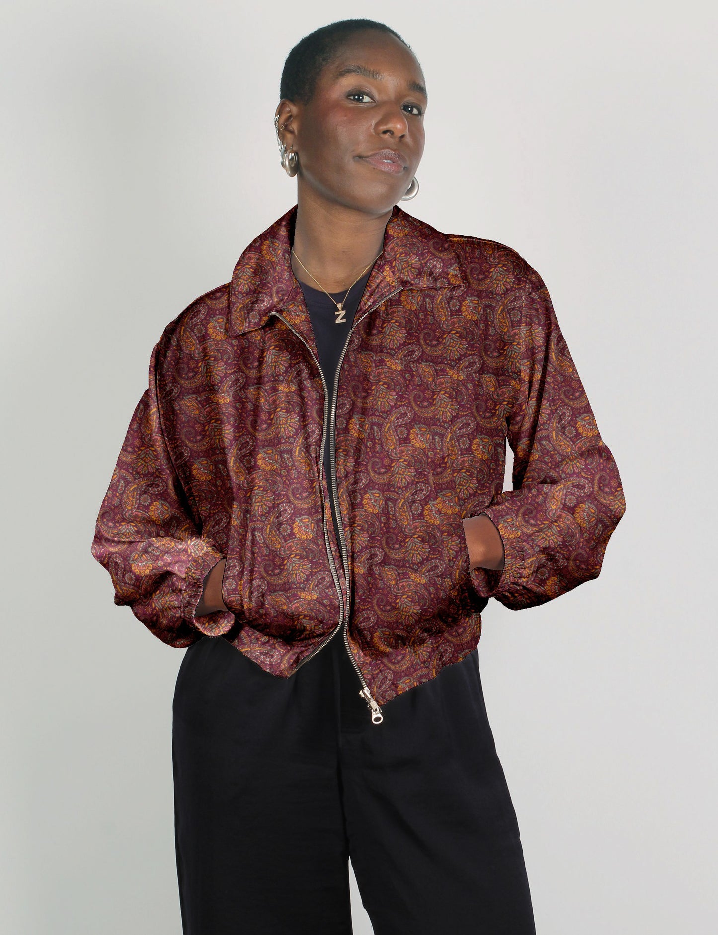 Woman wearing a red paisley bomber jacket with zipper front and elastic cuffs, paired with black pants, front view