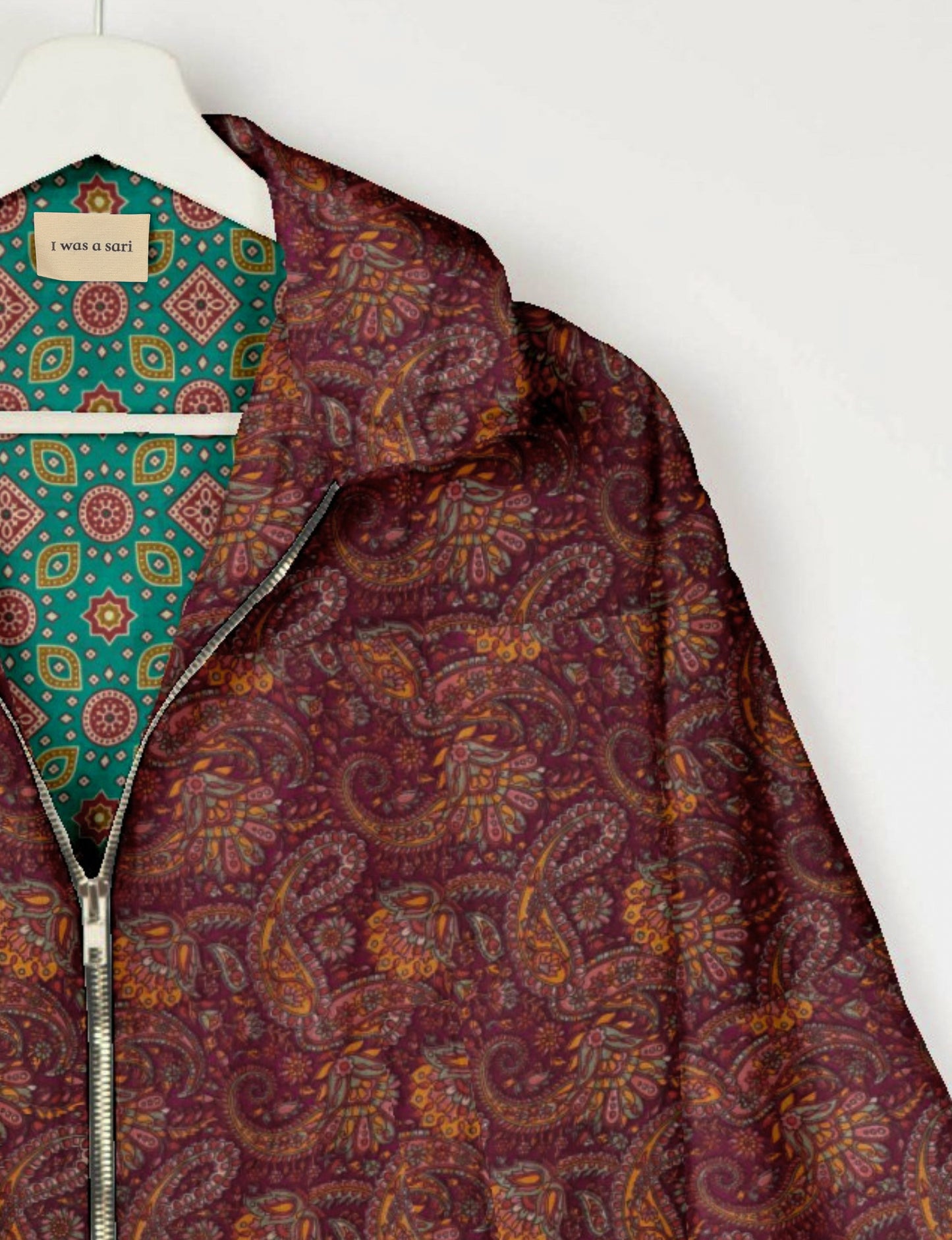 Red paisley patterned bomber jacket with silver zipper, shown partially unzipped on a white hanger with green patterned