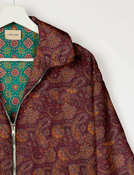 Red paisley patterned bomber jacket with silver zipper, shown partially unzipped on a white hanger with green patterned
