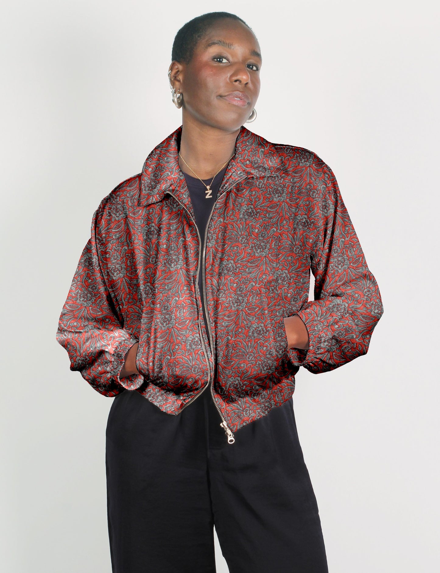 Woman wearing a red tropical patterned bomber jacket with front zipper and elastic cuffs, paired with black pants