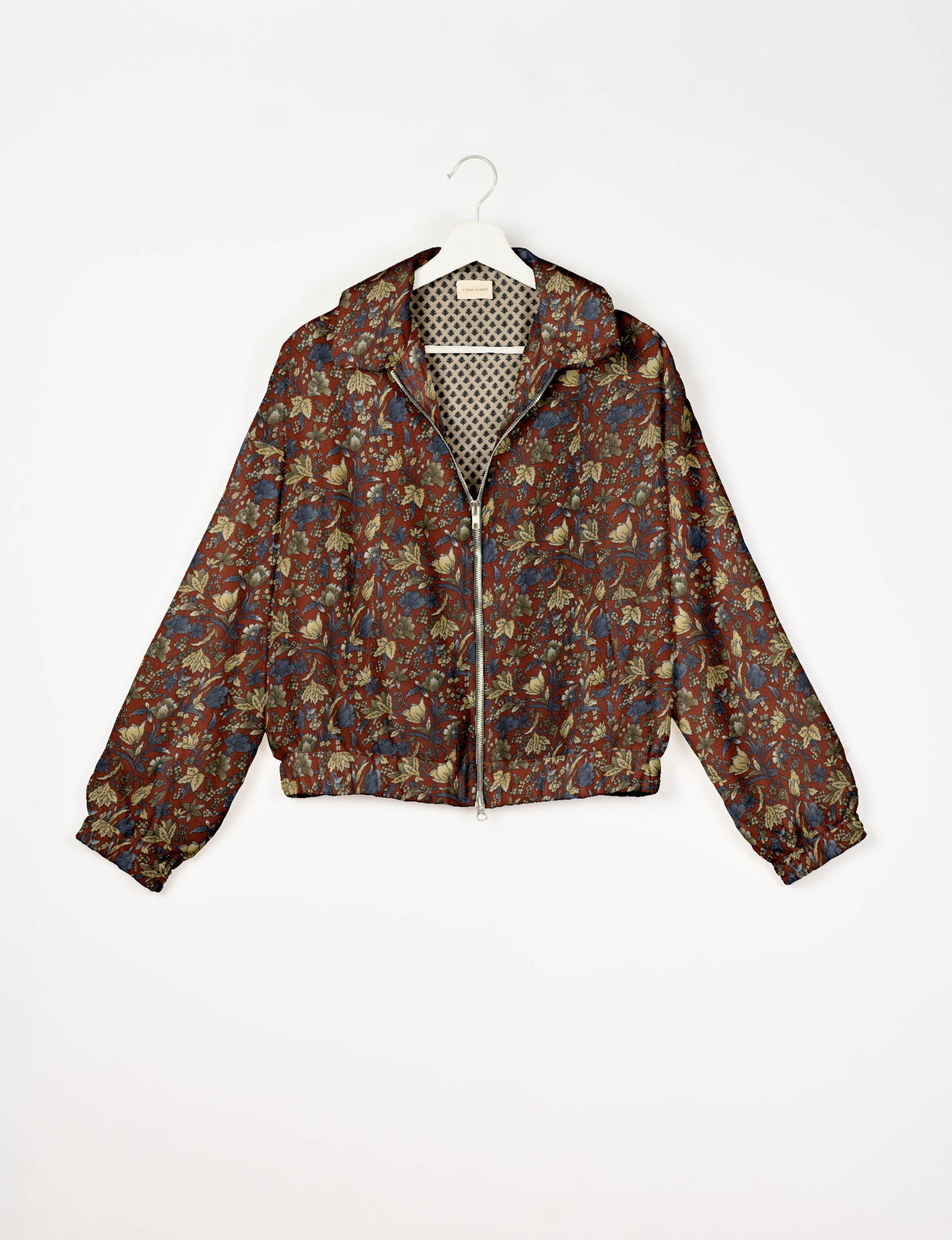 Floral patterned bomber jacket in rust, blue, and beige tones with front zipper and elastic cuffs, shown hanging on white