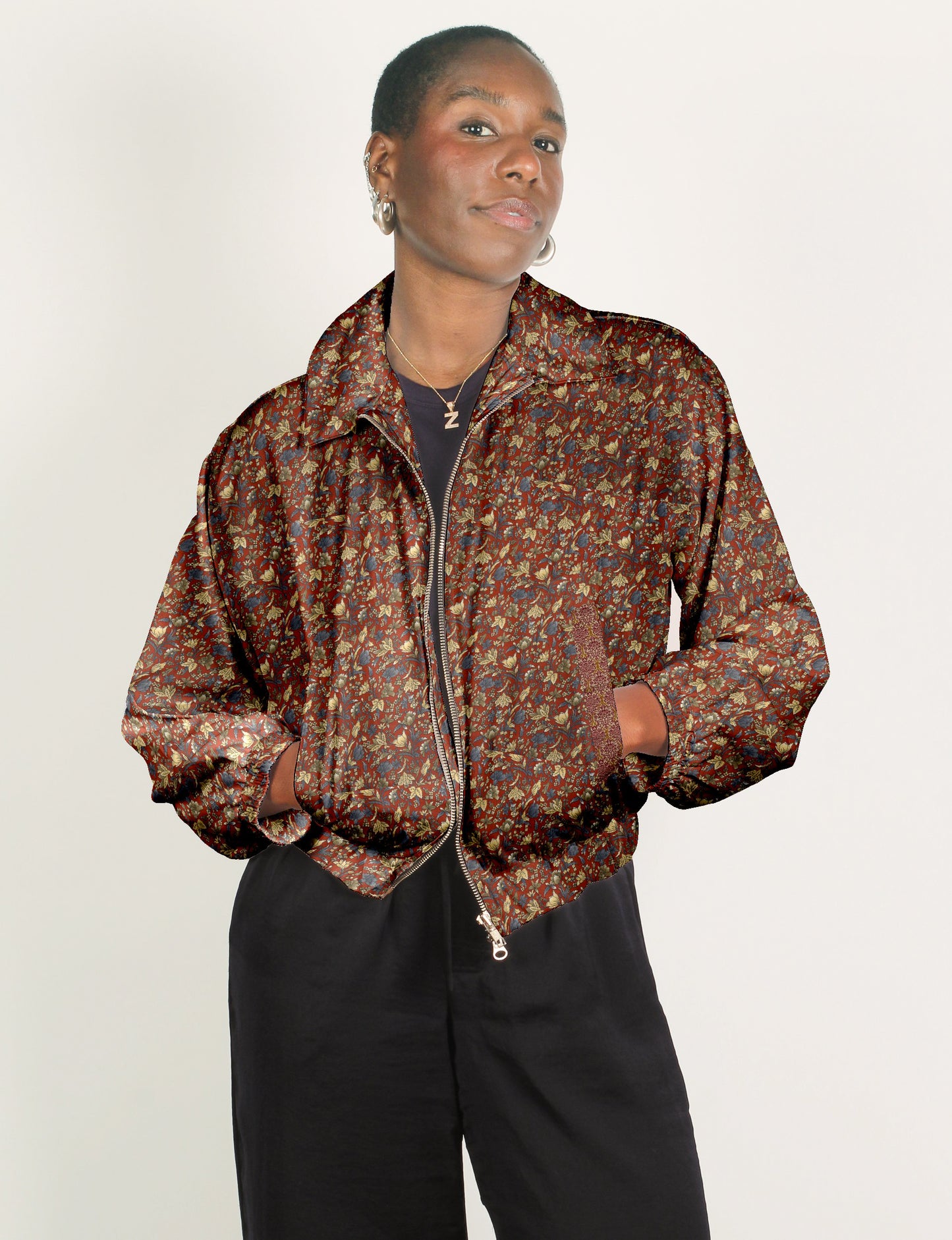 Woman wearing a red floral patterned bomber jacket with a front zipper and elastic cuffs, paired with black pants