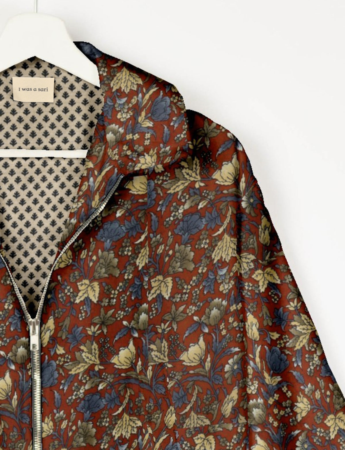 Floral patterned bomber jacket in rust, blue, and beige with silver zipper, shown on hanger with patterned lining and label