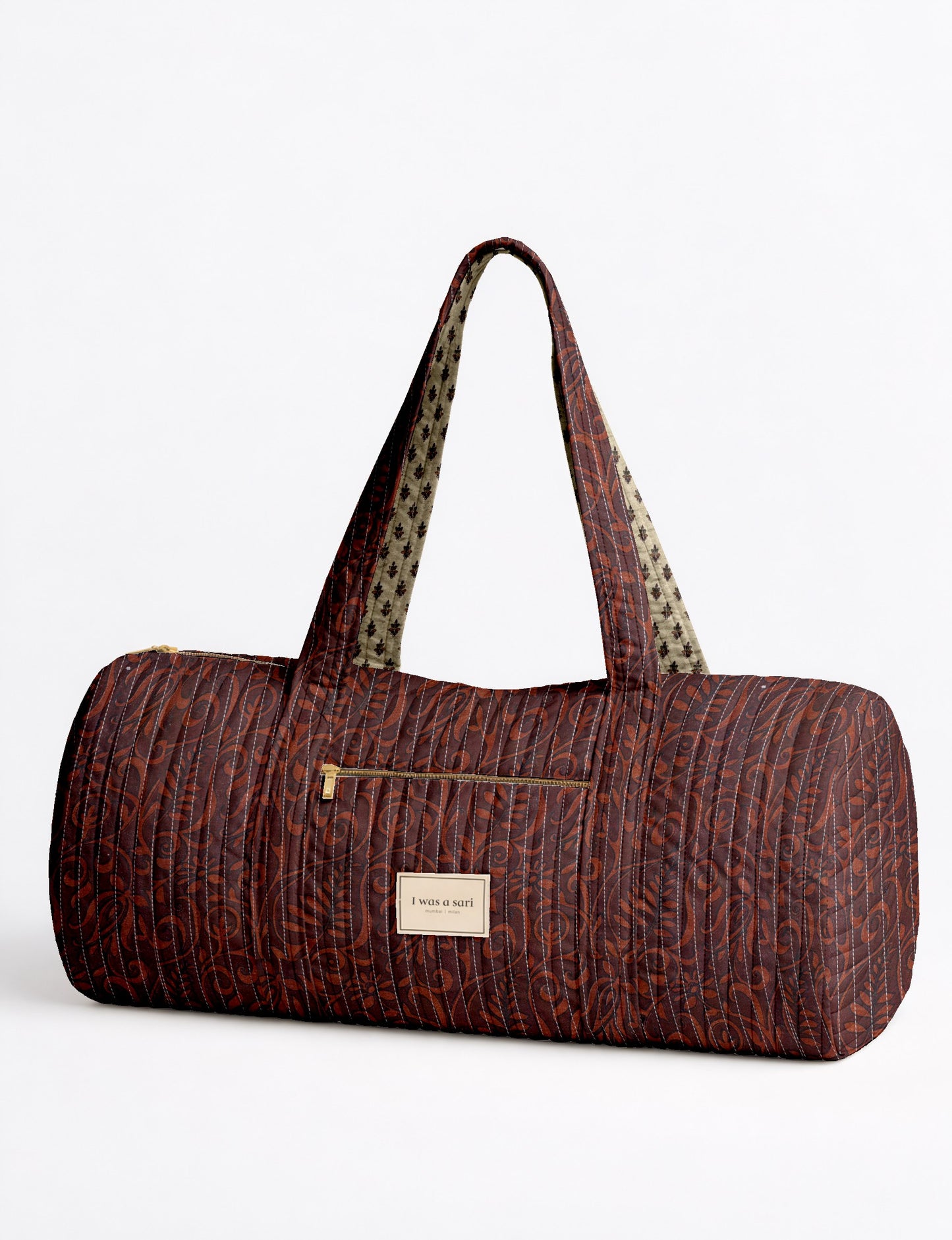 Quilted bowling bag by I Was A Sari with a structured design, featuring dual handles, zip closure, and a spacious interior with an outer zip pocket. Designed for everyday use and travel, it showcases a sleek elongated silhouette with functional storage and easy access compartments. Made from upcycled fabric, this sustainable handbag combines style and practicality, presented through detailed front, side, and lifestyle views.