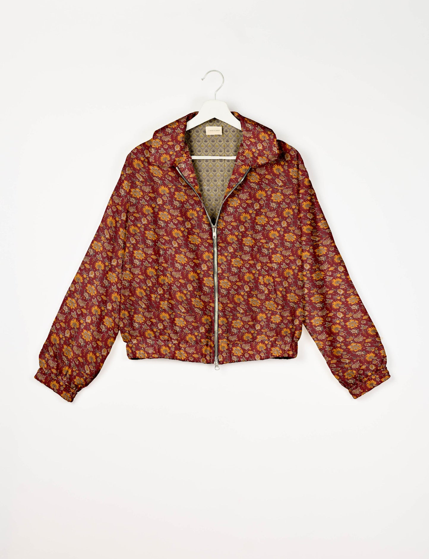 Red bomber jacket with yellow and orange floral print, front zipper, elastic cuffs, and patterned inner lining, hanging on