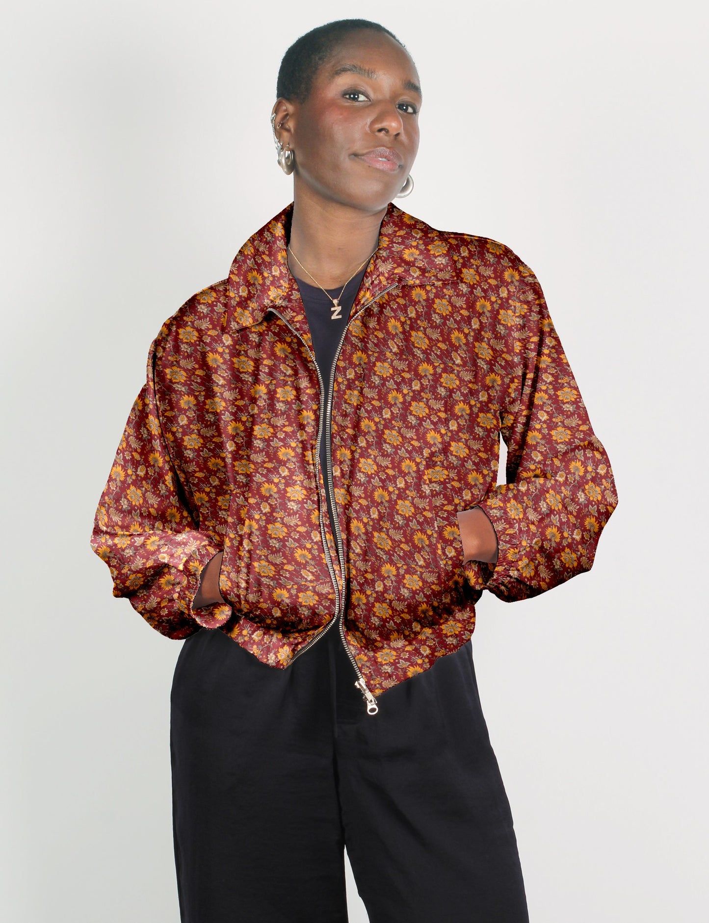 Woman wearing a red tropical floral bomber jacket with a front zipper and elastic cuffs, paired with black pants