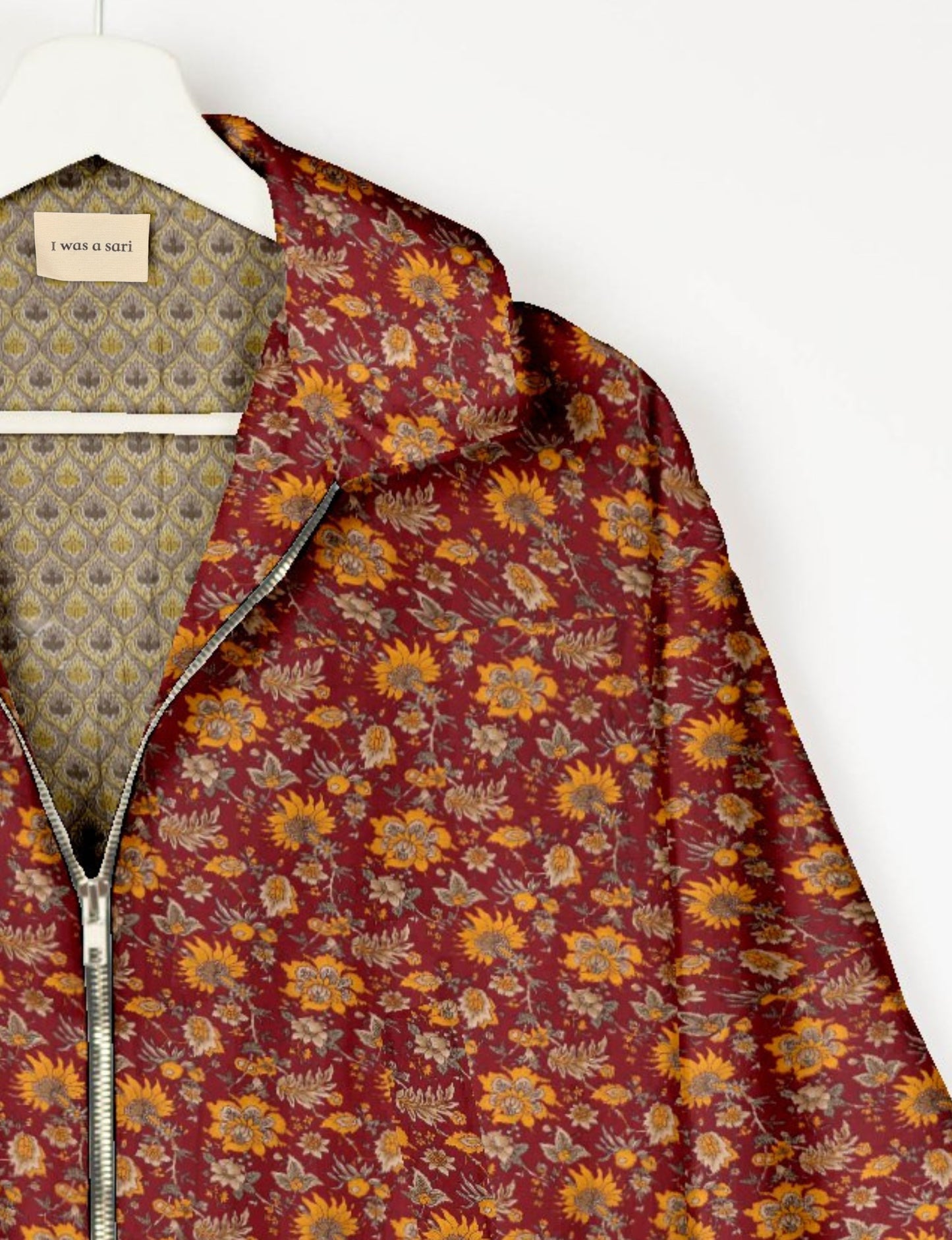 Red floral bomber jacket with yellow and beige flowers, silver zipper, and patterned inner lining on white hanger with "I