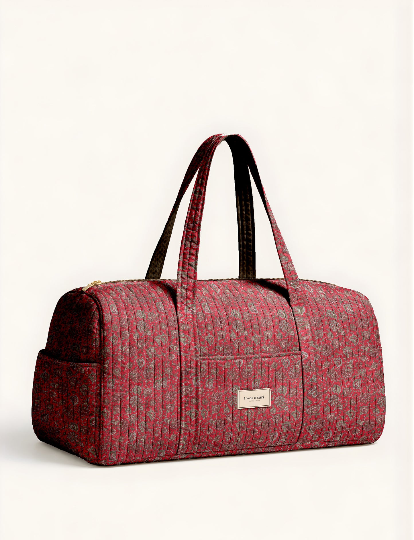 Quilted brown paisley barrel bag with double handles, front pocket, and gold zipper, shown in side angle view