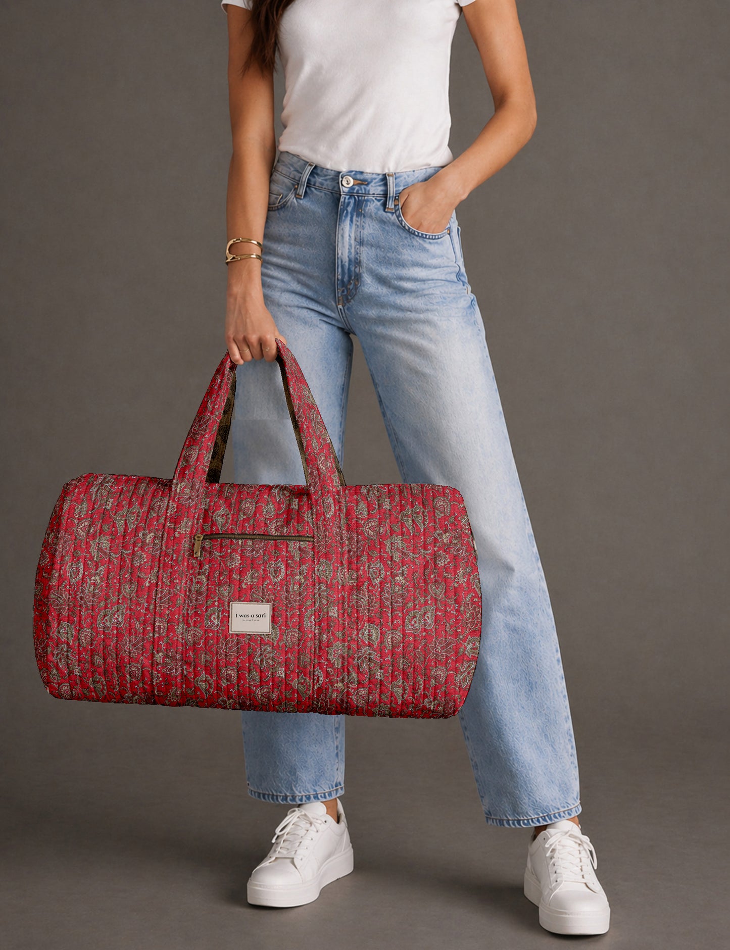 Woman holding a brown paisley quilted barrel bag with front zipper pocket, wearing light blue jeans and white sneakers
