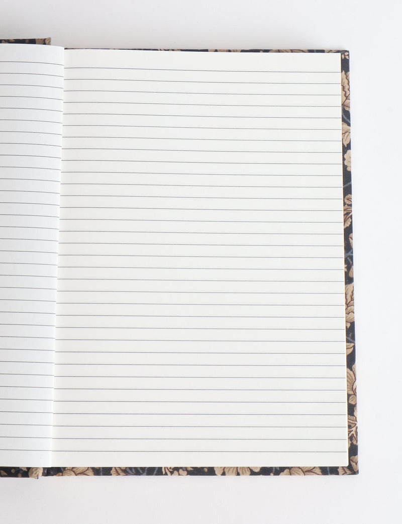 Open A5 hard cover notebook with blue and beige floral patterned edges and lined white pages, flat lay view