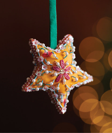 Yellow fabric star ornament with pink and white bead embroidery, hanging from a green ribbon against a dark background