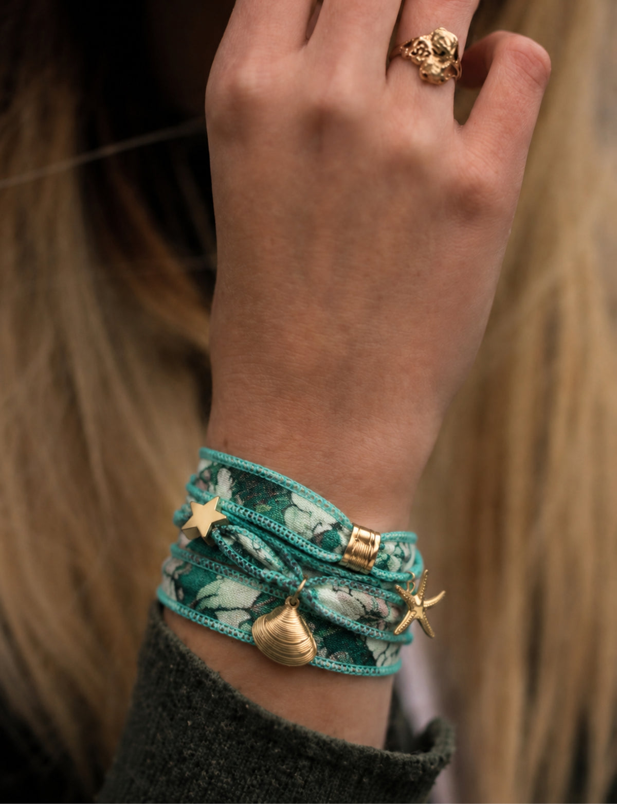 Turquoise wrap-around bracelet with floral pattern and gold-tone star, shell, and starfish charms worn on wrist