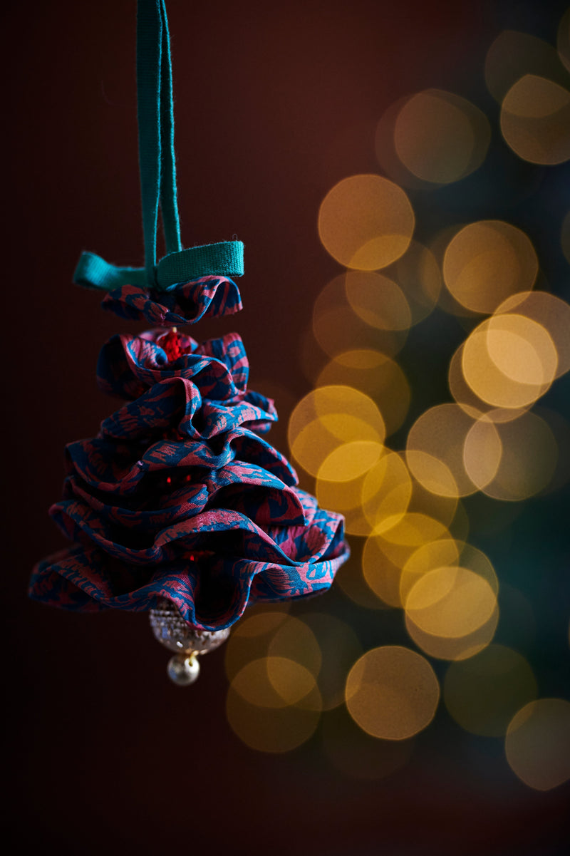 Hanging fabric Christmas tree ornament with blue and red abstract pattern and pearl bead at the bottom against blurred lights