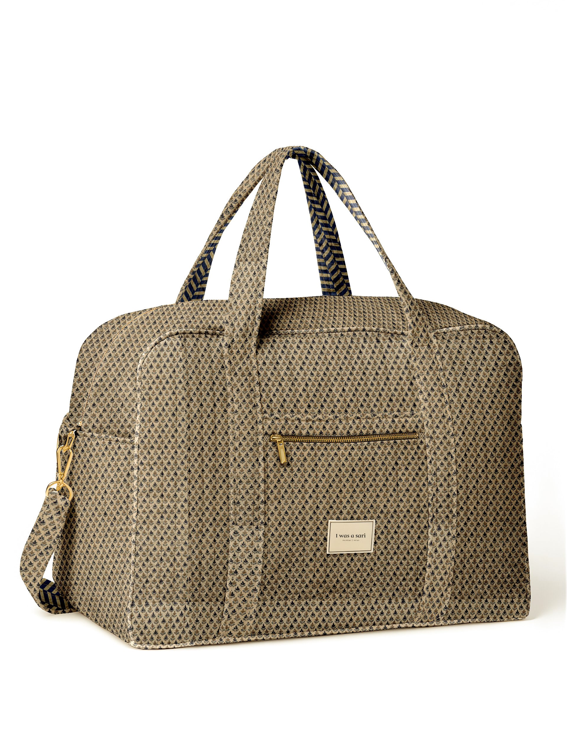 Beige quilted duffle bag with micro floral pattern, front zip pocket, dual handles, and "I was a sari" label on front