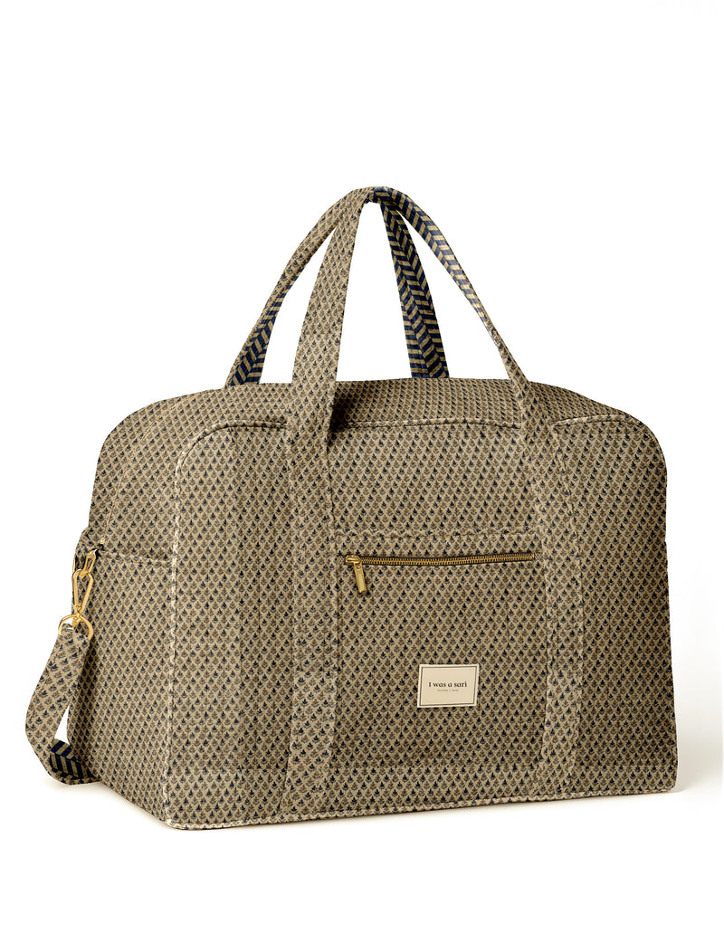 Beige quilted duffle bag with micro floral pattern, front zip pocket, dual handles, and "I was a sari" label on front