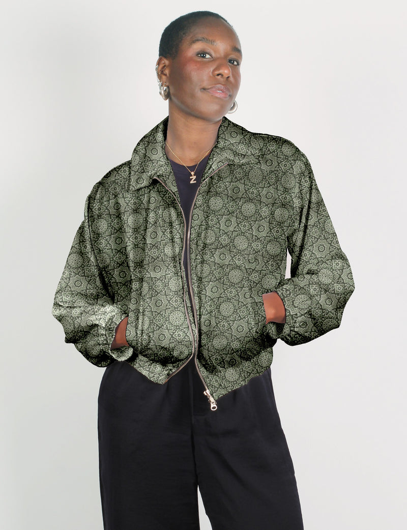 Green bomber jacket with Indian ethnic pattern, front zipper, collar, and elastic cuffs, worn by model with hands in pockets