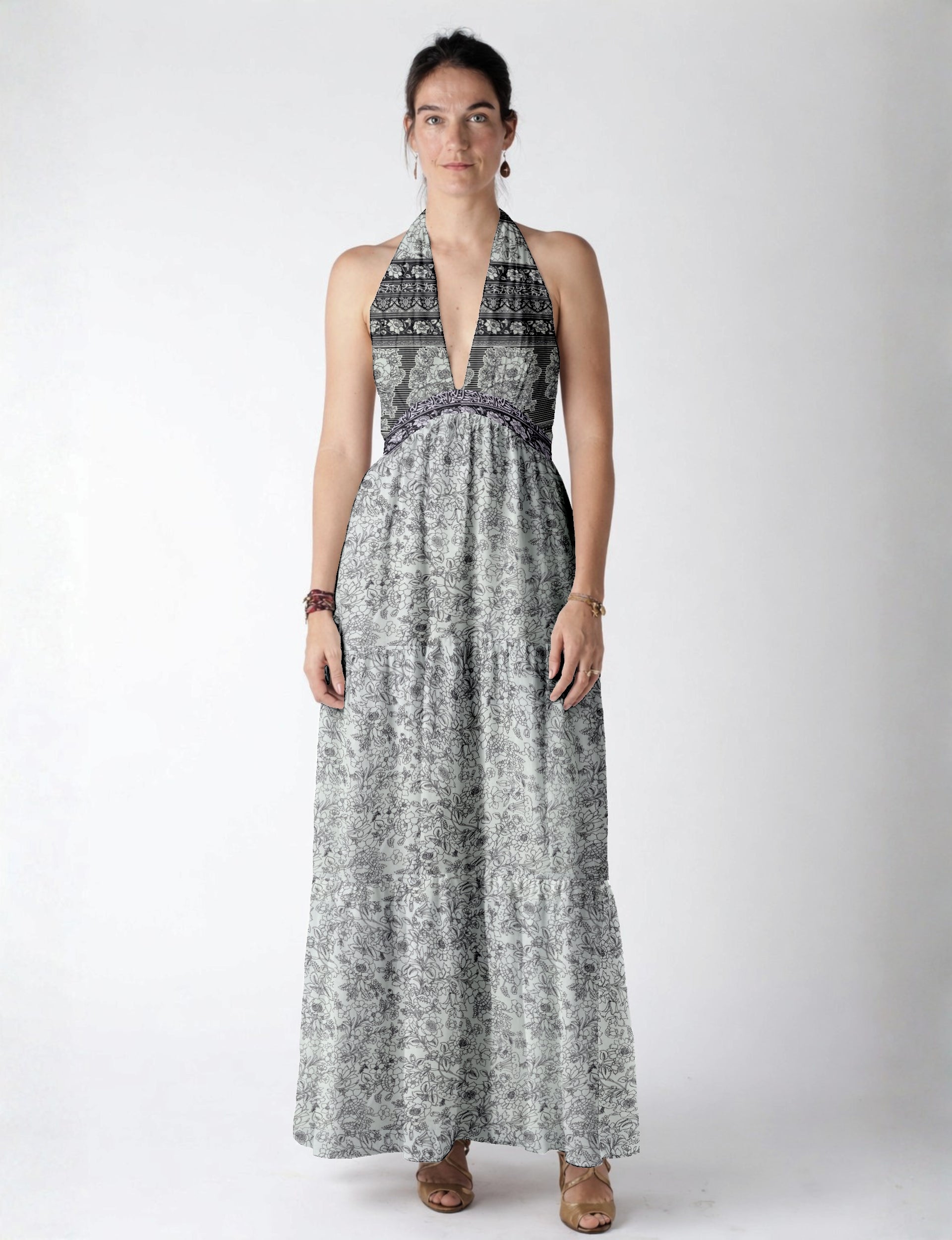 Woman wearing a white maxi tiered dress with black floral and stripe patterns, halter neckline, and deep V front view