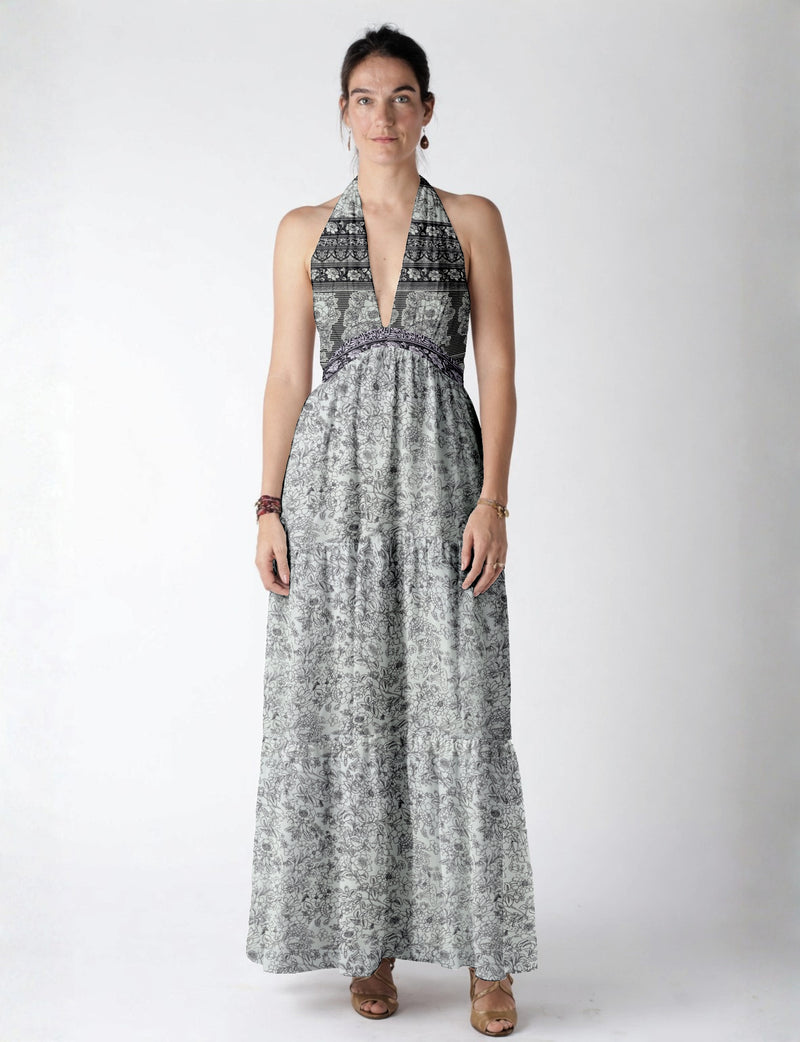 Woman wearing a white maxi tiered dress with black floral and stripe patterns, halter neckline, and deep V front view