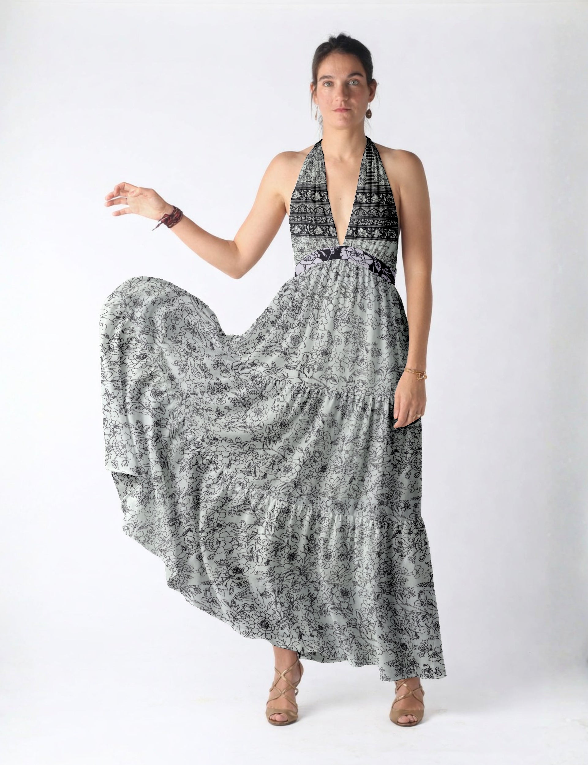Woman wearing a white maxi tiered dress with black floral and geometric patterns, halter neckline, and beige strappy heels