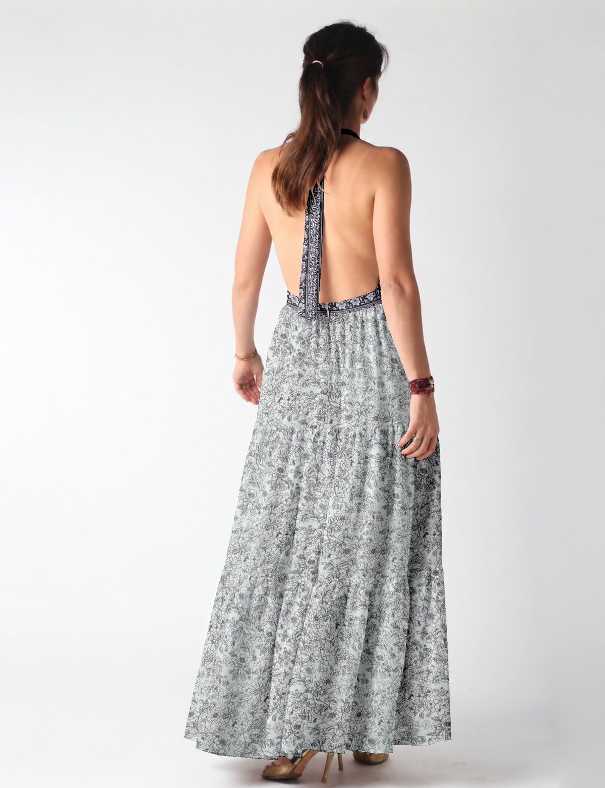 Woman wearing white maxi tiered dress with black floral print and halter neck tie, shown from back view