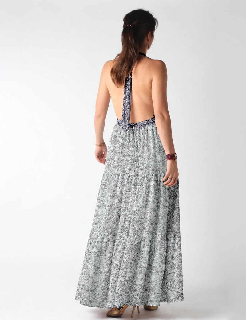 Woman wearing white maxi tiered dress with black floral print and halter neck tie, shown from back view