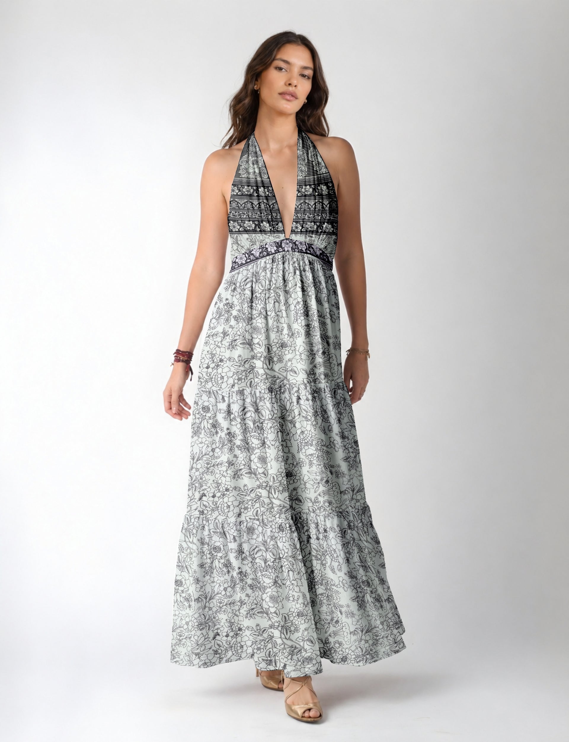 Woman wearing a white maxi tiered dress with black floral and geometric patterns and a deep V halter neckline, front view