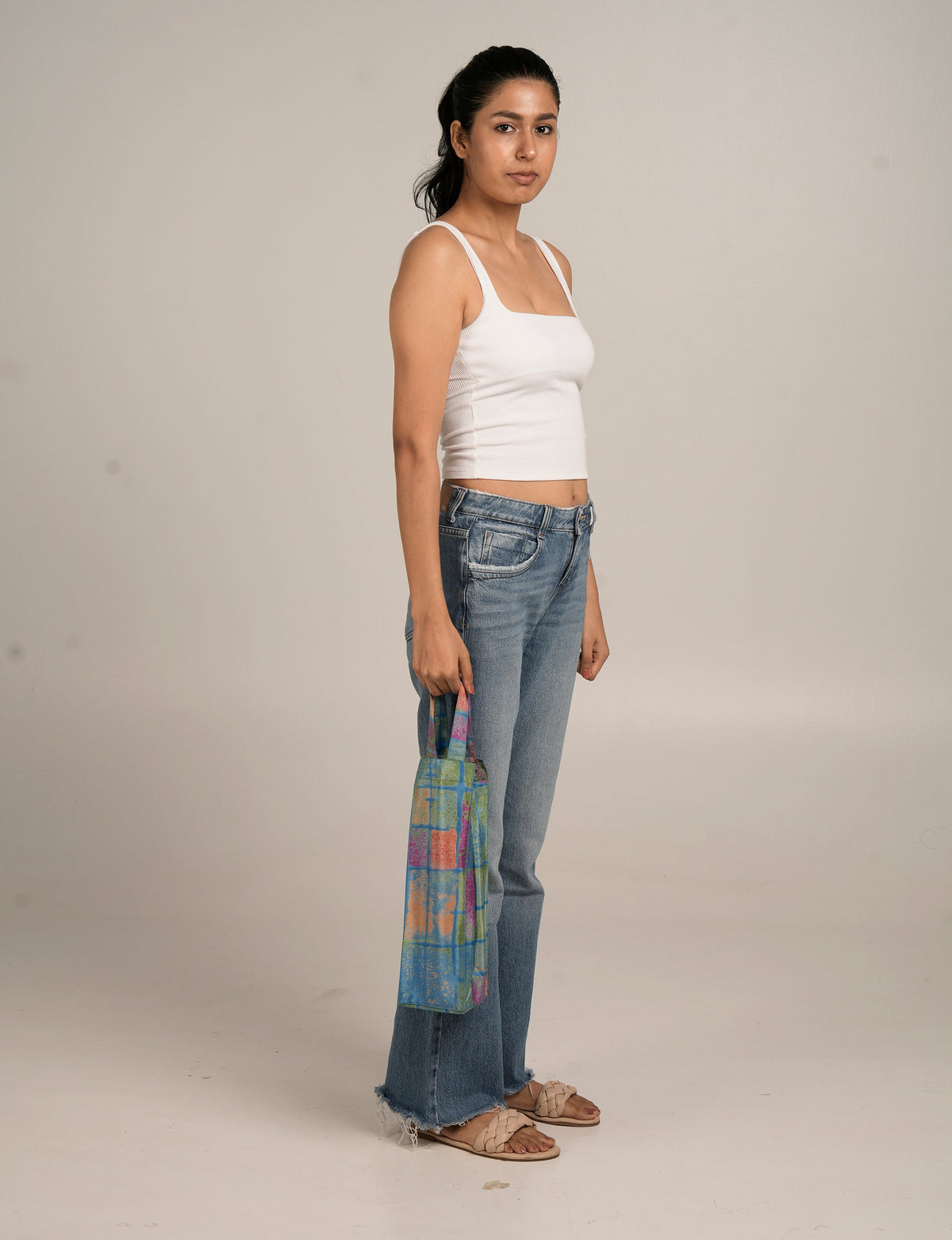Model wearing a multicolor checkered wine bag with blue, green, orange, and pink squares, held by short handles at side