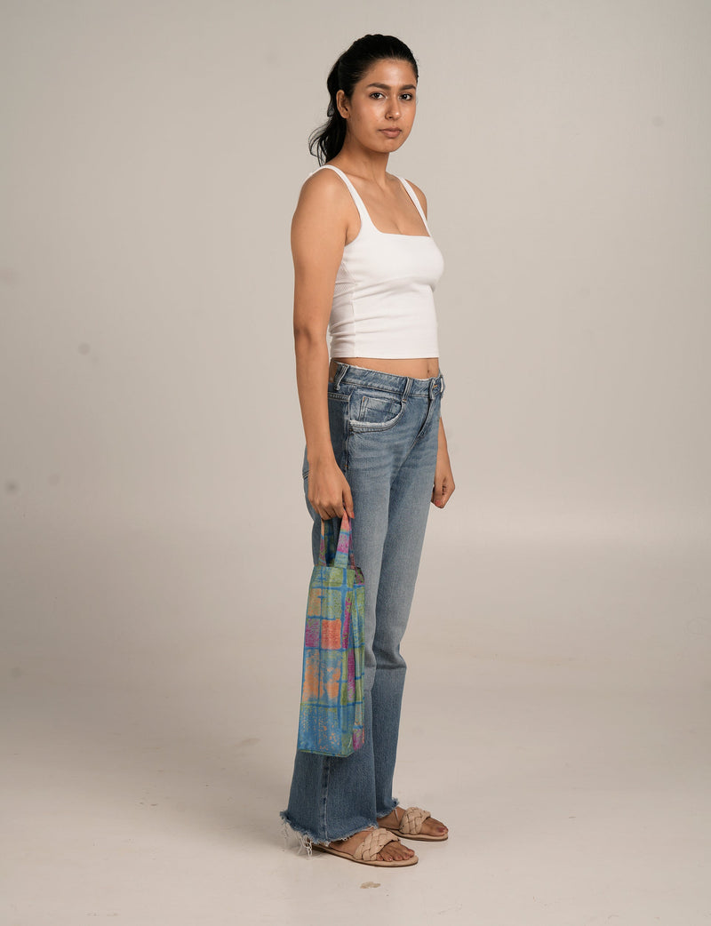Model wearing a multicolor checkered wine bag with blue, green, orange, and pink squares, held by short handles at side