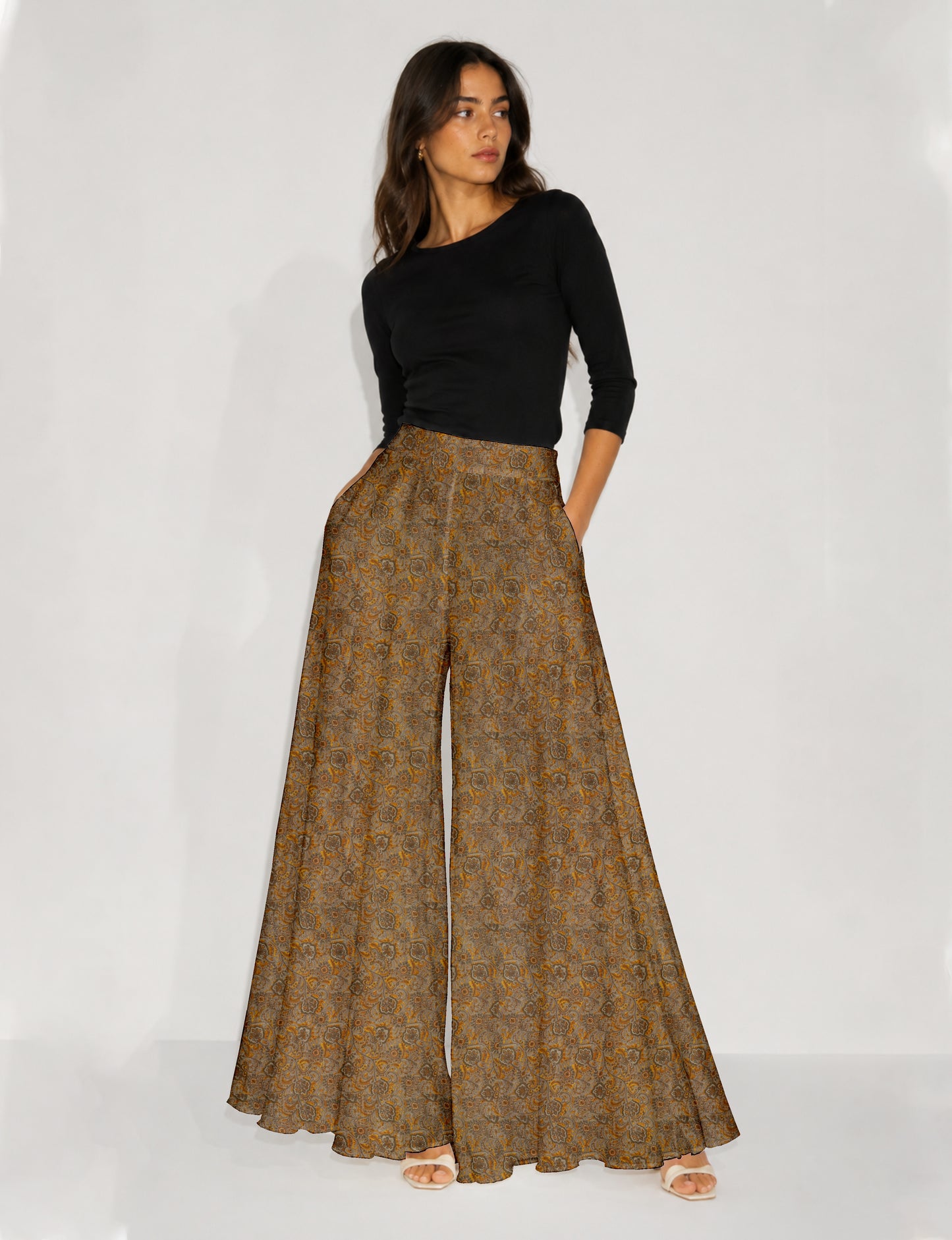 Woman wearing blue wide leg palazzo trousers with black and brown tropical floral print, side pockets, shown from back angle