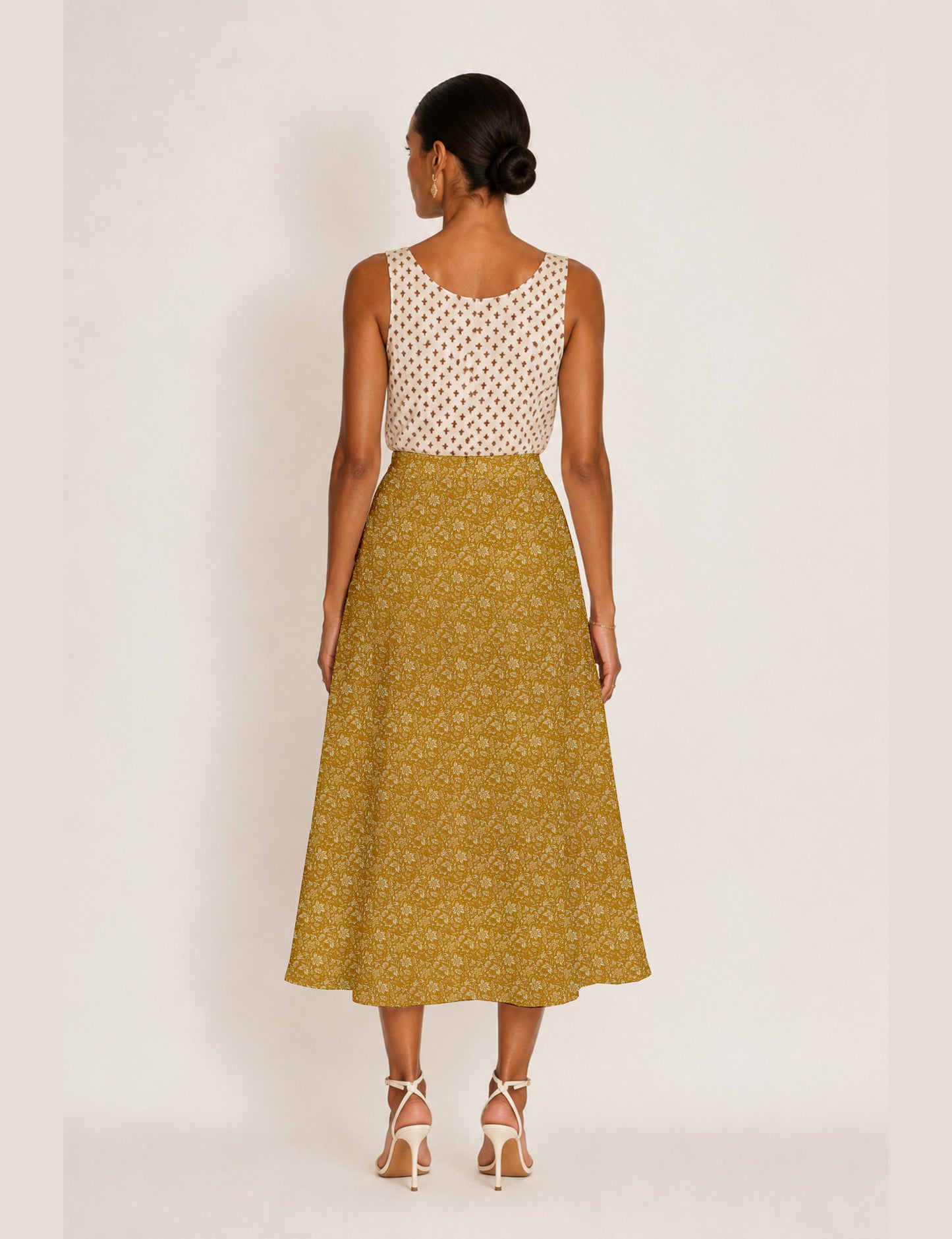 Woman wearing a yellow and black micro patterned A-line skirt with front slit, paired with beige sleeveless top and black