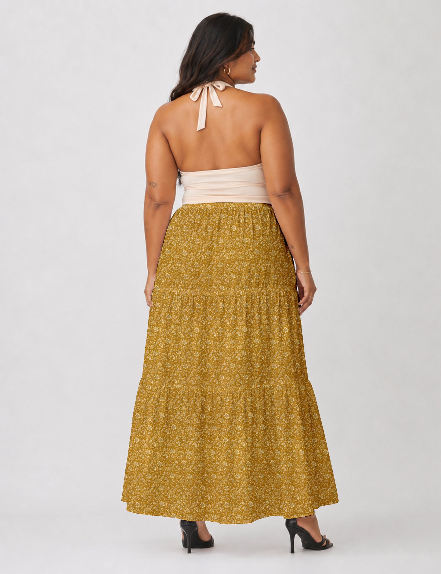 Woman wearing a yellow midi tiered skirt with a small geometric pattern, paired with a beige strapless top and white heels